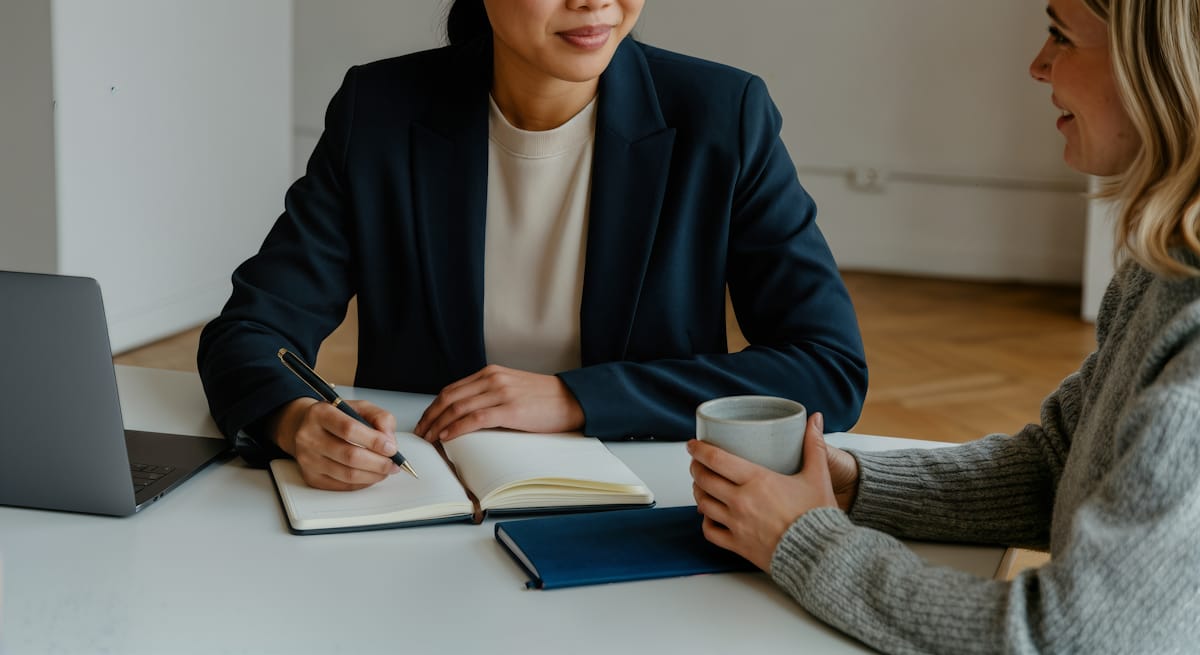 A one-on-one customer interview across a table, notes in progress