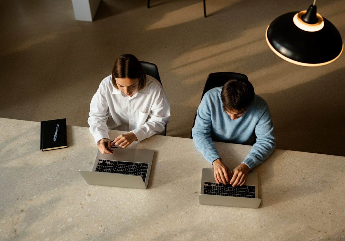 Two people working side by side at laptops, seen from above